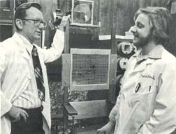 Dr. Frank R. Hendrickson (left) and Brian Pientak, radiation
 therapy technologist, in the Cancer Therapy Facility at 
 Fermilab. They are in the shielded room in which patients 
 are exposed to neutrons. The patients sit in the chair 
 between them. Just above Hendrickson's left hand is a
 laser device that technologists use to precisely align a 
 patient with the neutron source